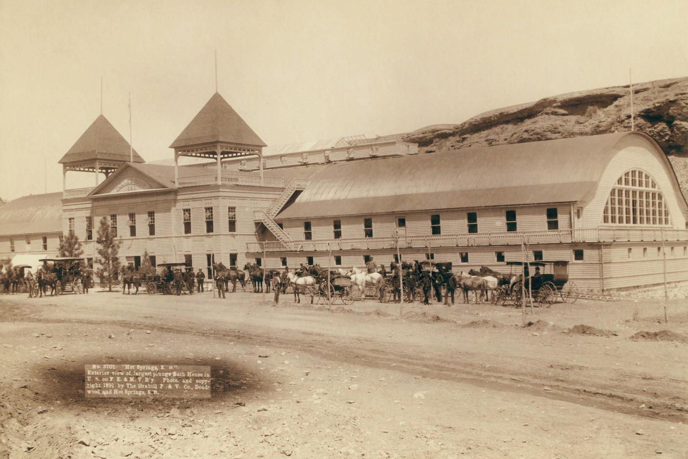 Hot Springs Bath House, United States, circa 1890: Exterior view of largest plunge bath house in U.S. on F.E. and M.V. Railway; Large building with several horses and carriages in front.