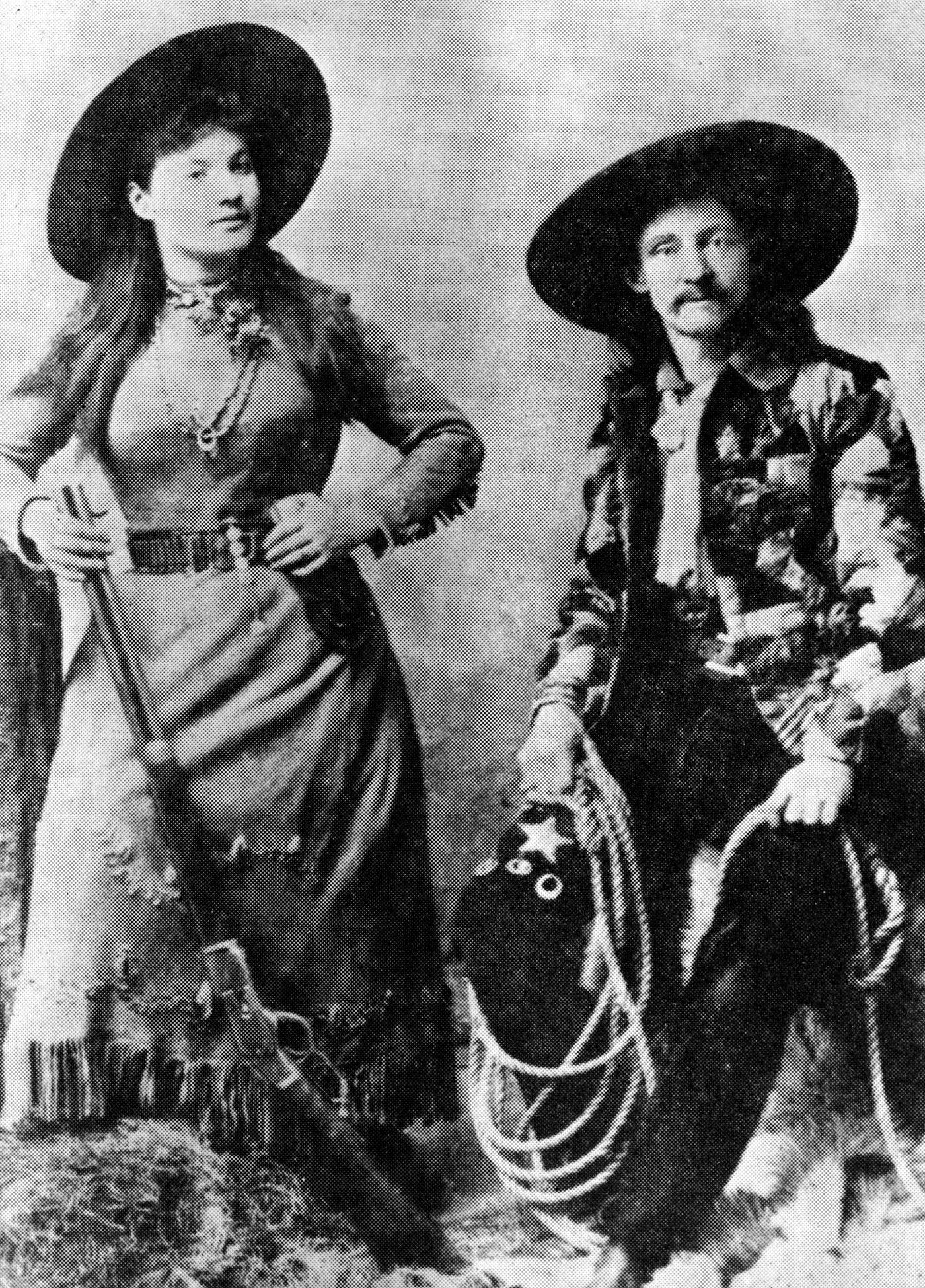 Publicity portrait of Annie Oakley & Texas Bill, late 1800s: American sharpshooter Annie Oakley (1860 - 1926) poses with one knee on a haybale and a shotgun on her hand, while Texas Bill Shufflebottom sits on a haybale with a lasso over his knee. The photograph was used to advertise her performances with Buffalo Bill's Wild West Show.