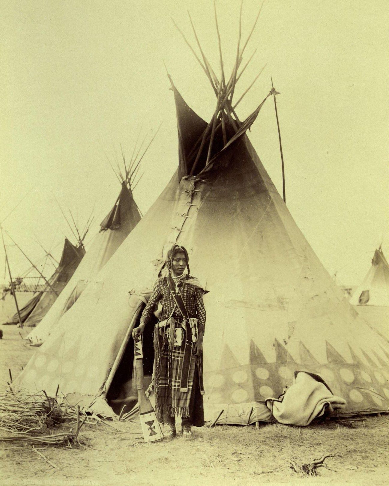 Blackfoot Brave, Montana, 1887: A young Native American warrior of the Blackfoot tribe stands in traditional clothing with a rifle in the entryway to his teepee home.