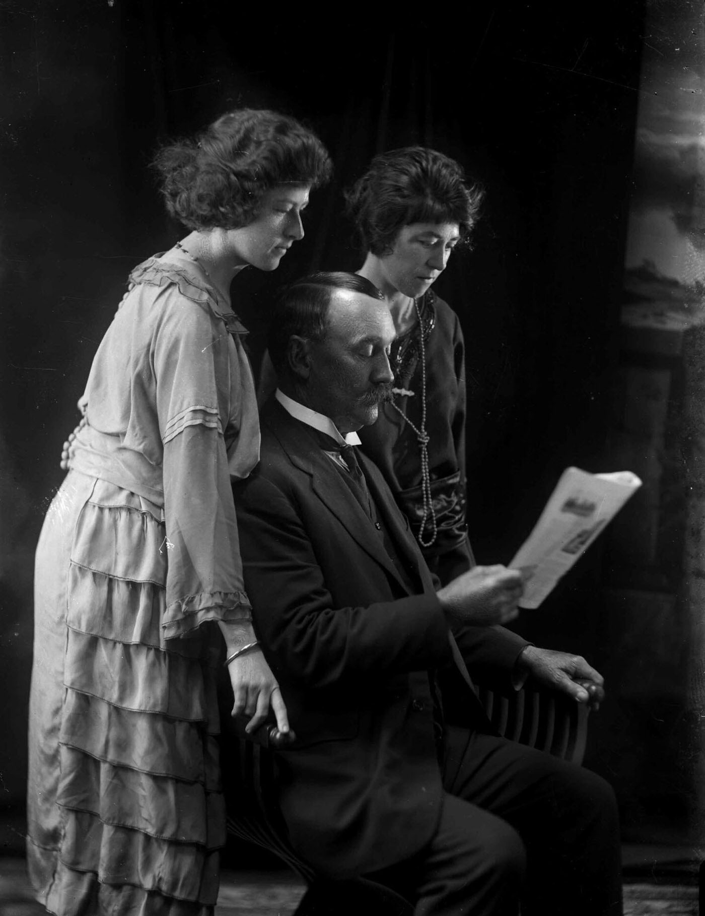 Group portrait featuring two ladies and a man reading a paper