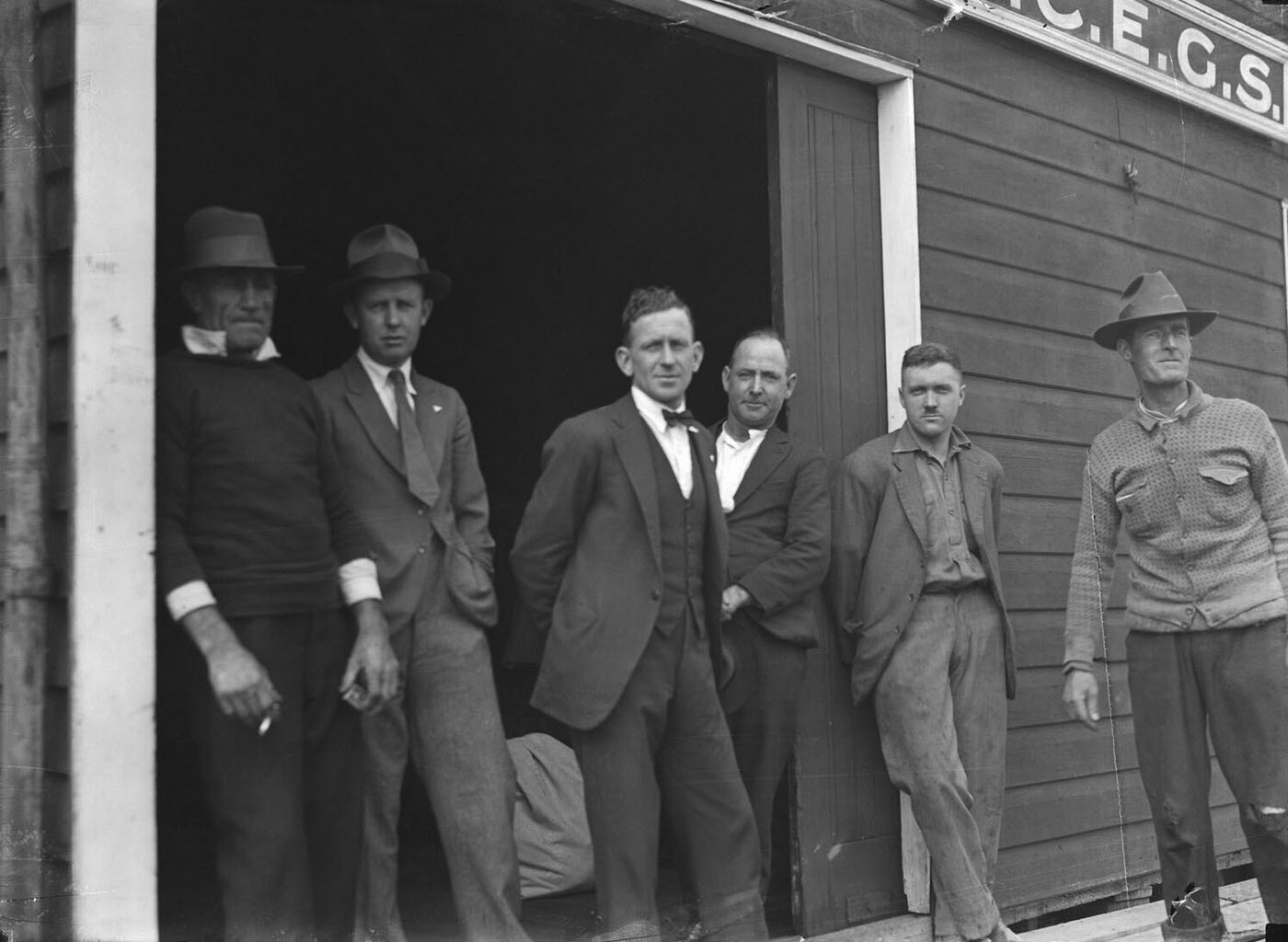 Portrait of six men standing outside SCEGS Boatshed, Berry's Bay