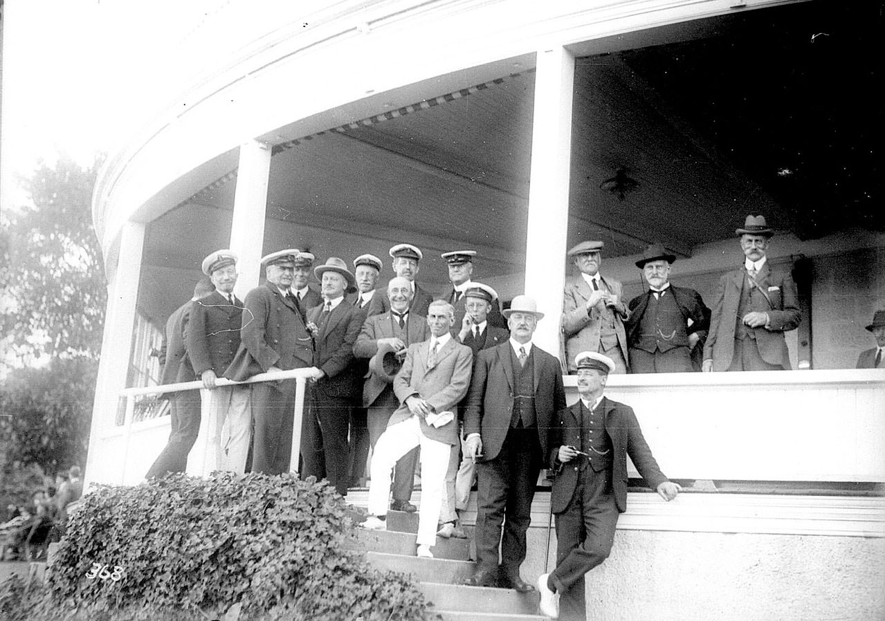 Men in yachting uniforms standing on the verandah of an unidentified yacht club
