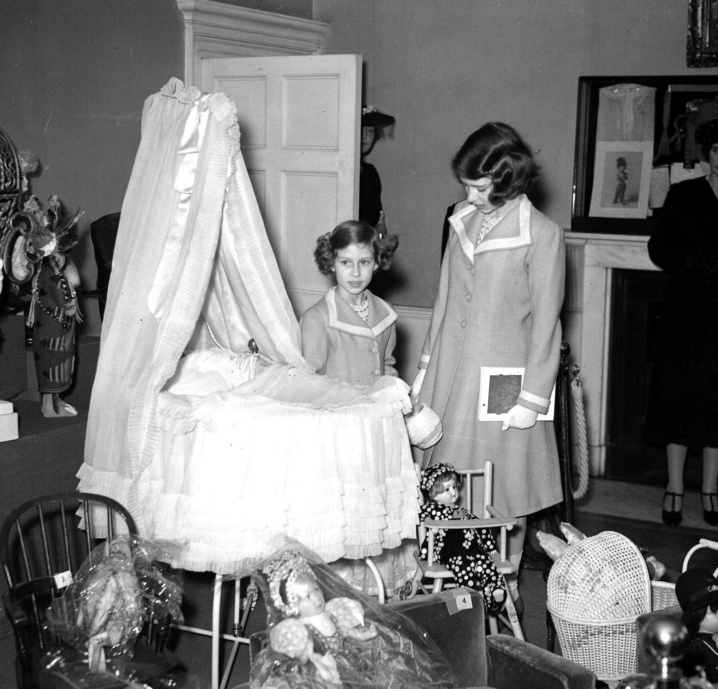 Princesses Elizabeth and Margaret view the cot that they both used as babies during their visit to an exhibition of royal and historic treasures at their old home, 145 Piccadilly, London, 28th July 1939.
