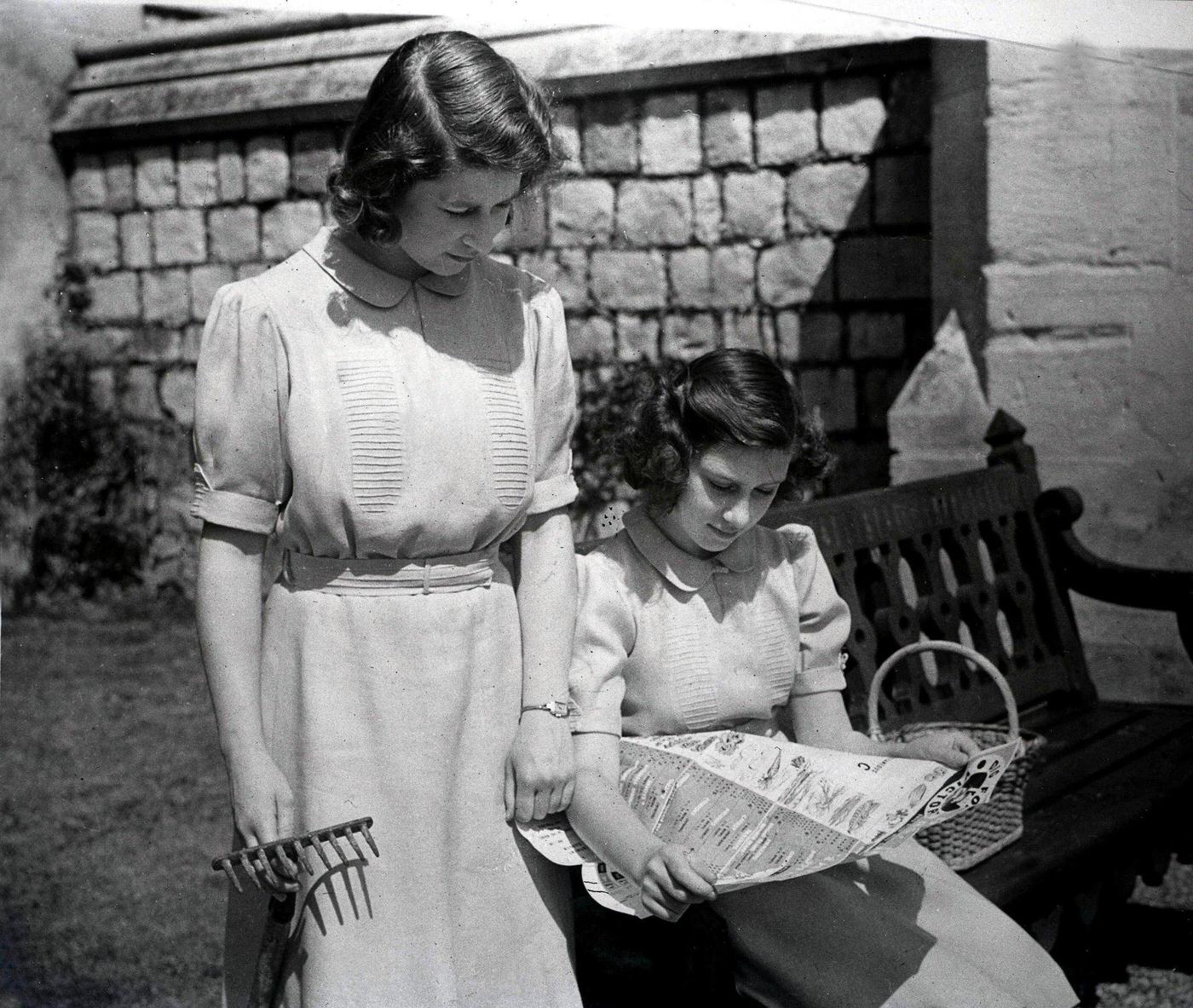 Princesses Elizabeth and Margaret study the Ministry of Agriculture's cropping chart in their allotments on the east side of Windsor Castle during World War Two, England, 1940's.