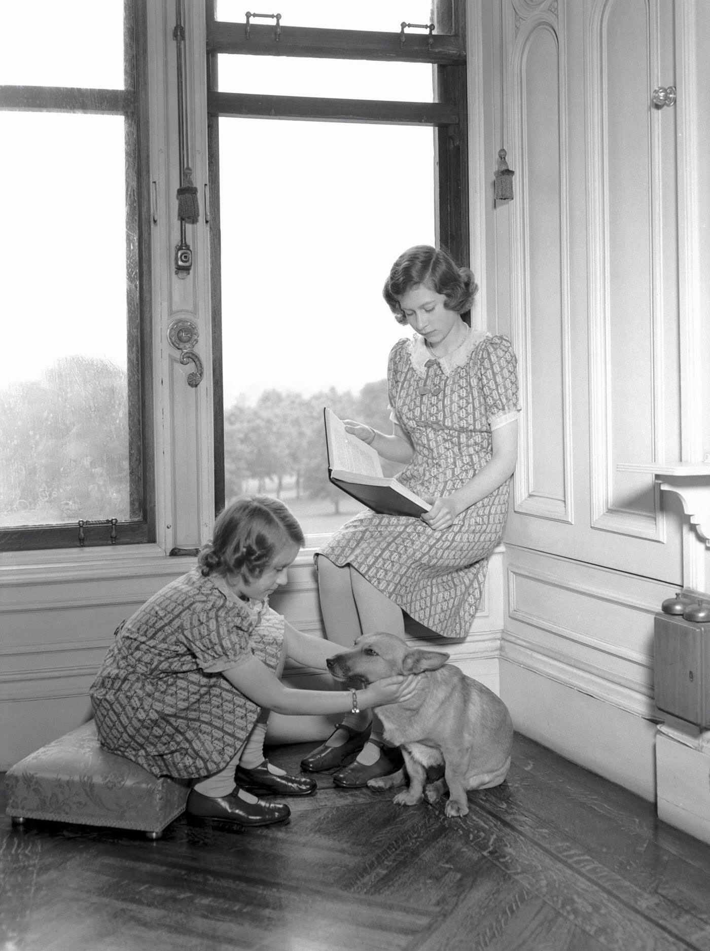 Princess Margaret plays with a corgi while Princess Elizabeth (later Queen Elizabeth II) reads at Windsor Castle, Berkshire, Great Britain, 22nd June 1940.