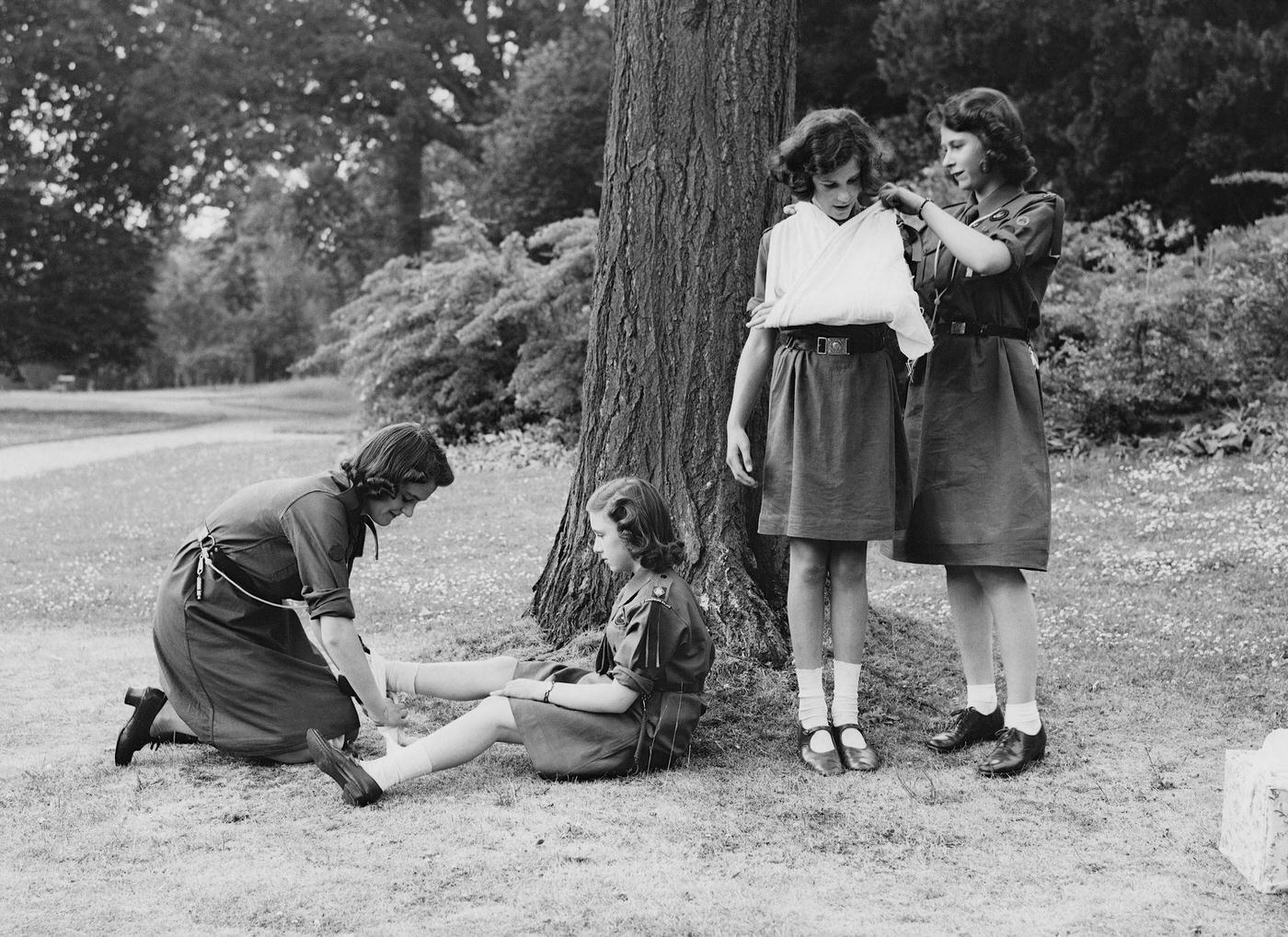 Princess Elizabeth places a young girl's arm in a sling as part of the girl guides in Frogmore, Windsor, England on April 11, 1942.