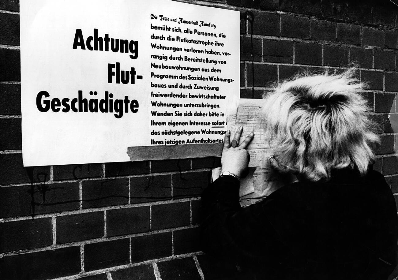 Woman in front of a sign in Wilhelmsburg during the North Sea Flood of 1962 in Hamburg, West Germany