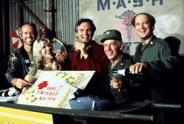 Mike Farrell, Loretta Swit, Alan Alda, Harry Morgan, and David Ogden Stiers raise a toast and a cake at a 7th anniversary cast party