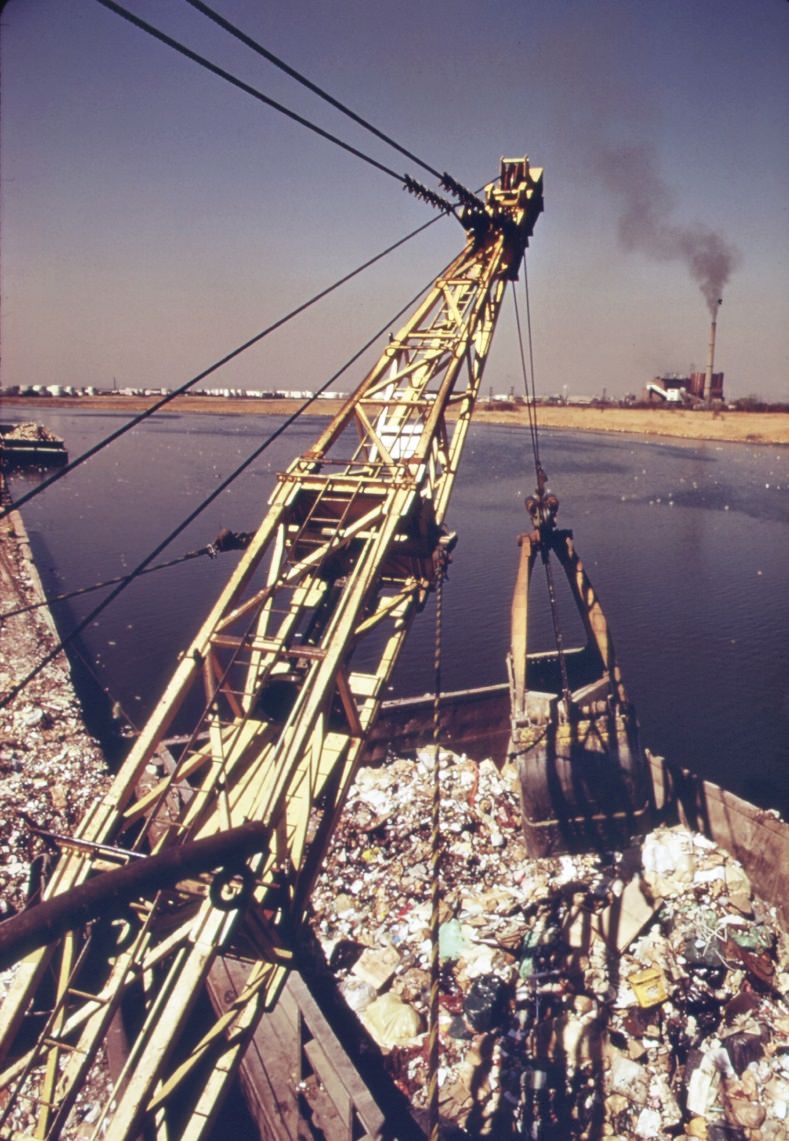 Unloading garbage scows at staten island. Carts haul the waste material to the edges of the vast landfill area. There the refuse is dumped and burned, 1970s