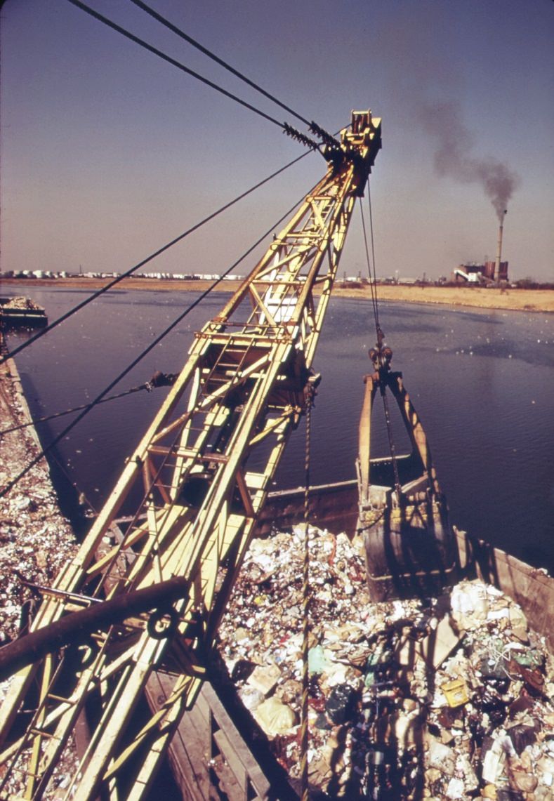 Unloading garbage scows at staten island. Carts haul the waste material to the edges of the vast landfill area. There the refuse is dumped and burned, 1970s