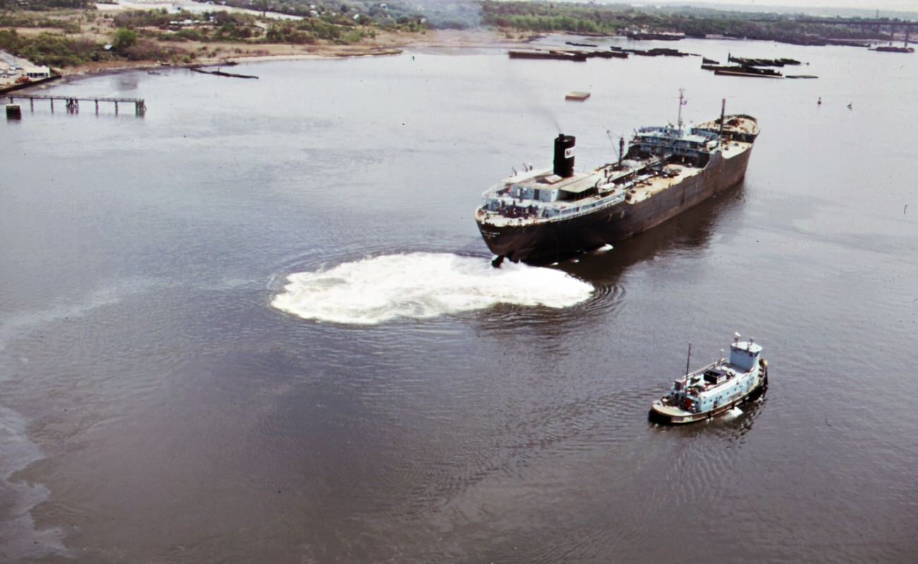 Mobile oil tanker and tug boat on arthur kill--the waterway between new jersey and staten island which is the site of a huge petrochemical manufacturing complex, 1970s