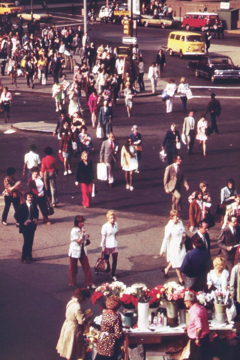 Commuters head for home at rush hour near the docks of the staten island ferries in battery park, lower manhattan. Some pause at a flower-sellers' stand, 1970s