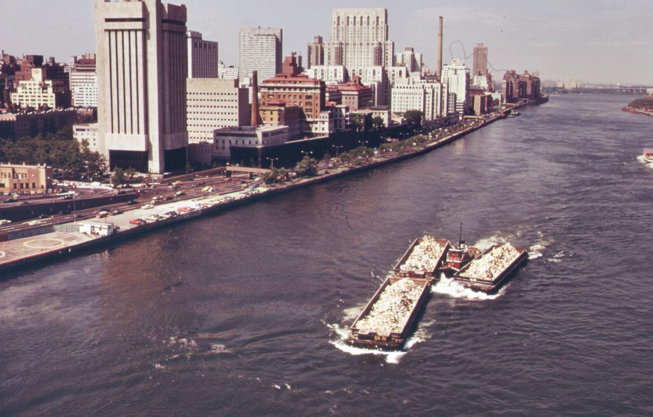 Part of the 26,000 tons of solid waste that new york city produces each day. Tugs tow heavily-laden barges down the east river to the overflowing staten island landfill, 1970s
