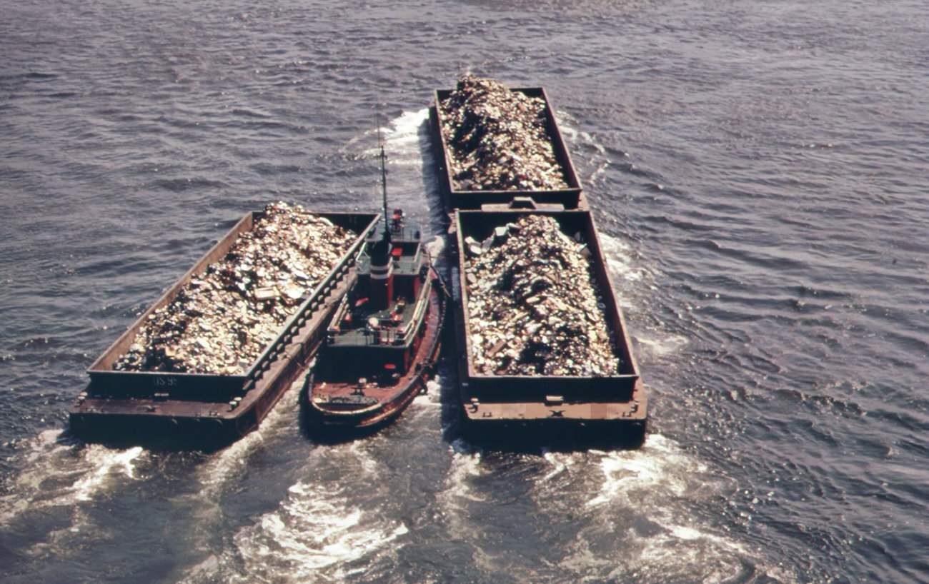 Part of the 26,000 tons of solid waste that new york city produces each day. Tugs tow heavily-laden barges down the east river to the overflowing staten island landfill, 1970s