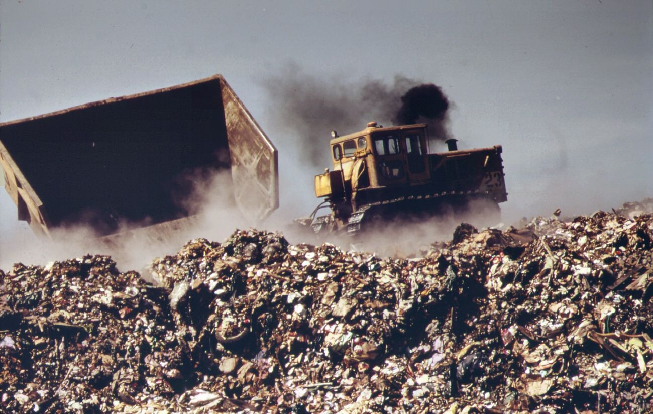 In last stage of city waste disposal process, garbage brought by barge from manhattan is dumped from carts at outer edges of staten island landfill. Previously deposited refuse is already smoldering, 1970s