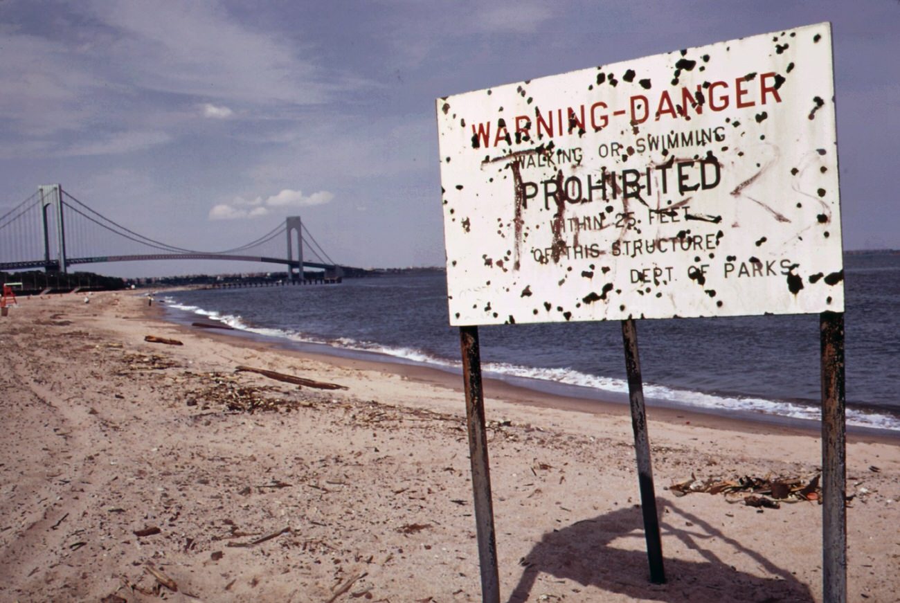 Warning of polluted water at staten island beach verrazano-narrows bridge in background, 1970s