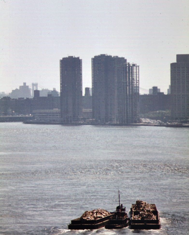 Tugboat tows garbage scows down the east river destination is the staten island landfill, 1970s