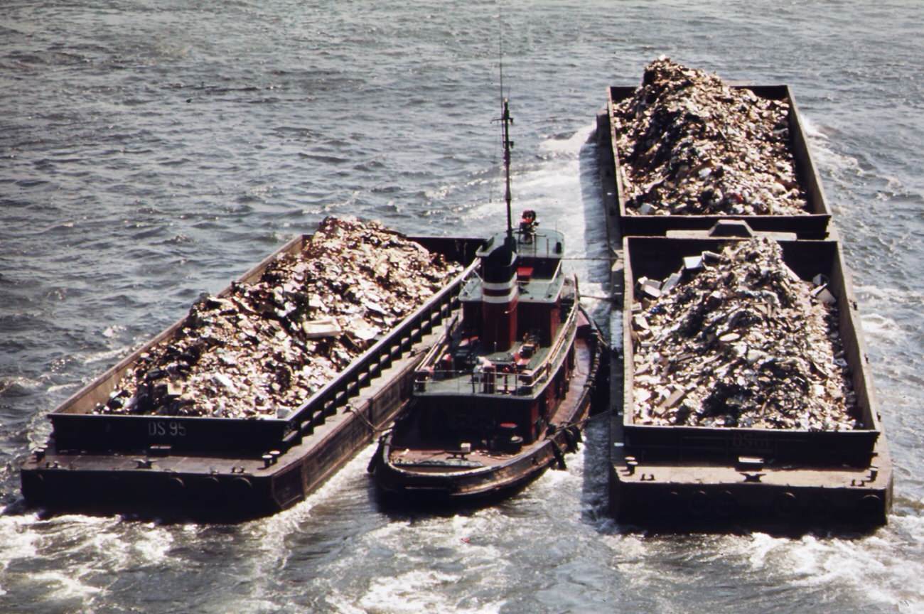 Tugboat herds garbage scows down the east river from a transfer point in manhattan. Destination is the staten island landfill, 1970s