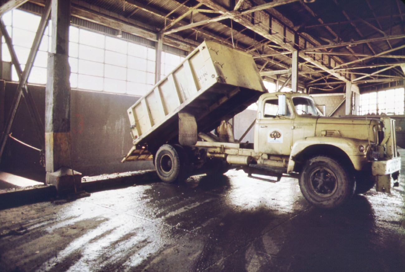 Truck at the 91st street marine transfer station empties garbage into barge for trip down the east river to the staten island landfill dumping site, 1970s