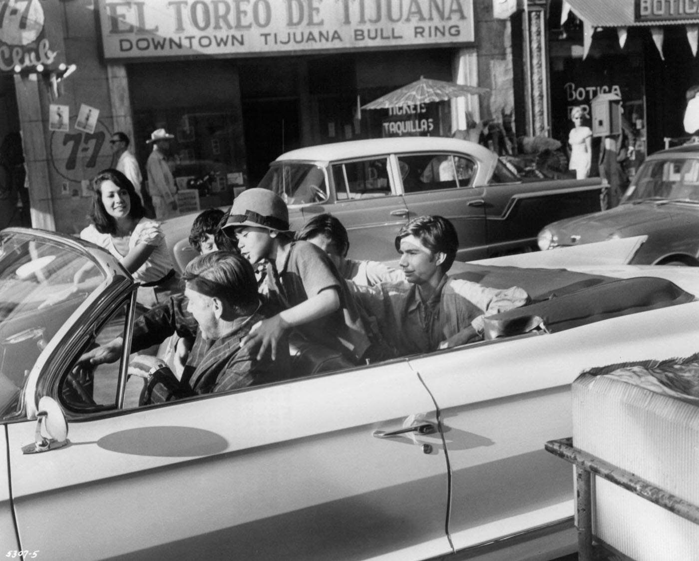 Crowd of actors in a convertible automobile riding down a street in downtown Tijuana in a scene from the film 'Dime With A Halo', 1963.