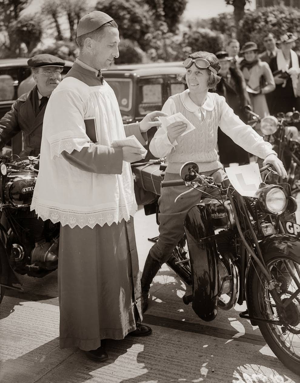 A reverend blesses the motorcycle of a woman who is learning to drive, 1938.