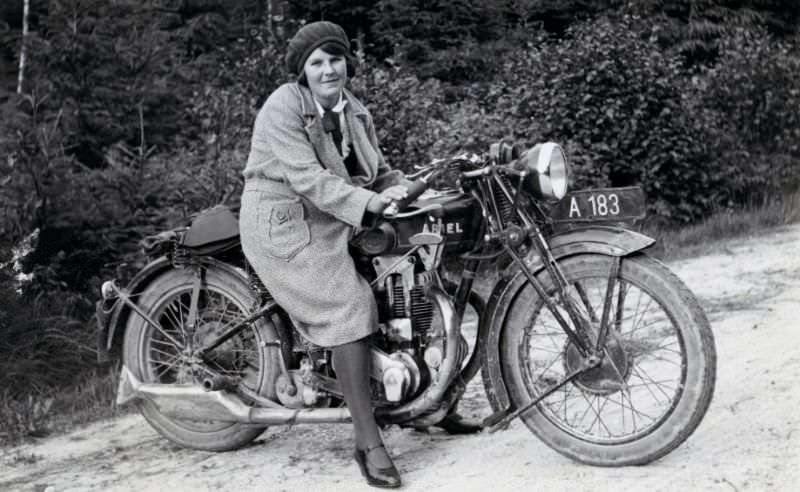 A fashionable lady posing in the saddle of an ariel model f 500 on a dirt road in the countryside. The bike is registered in the city of vienna, circa 1930s.