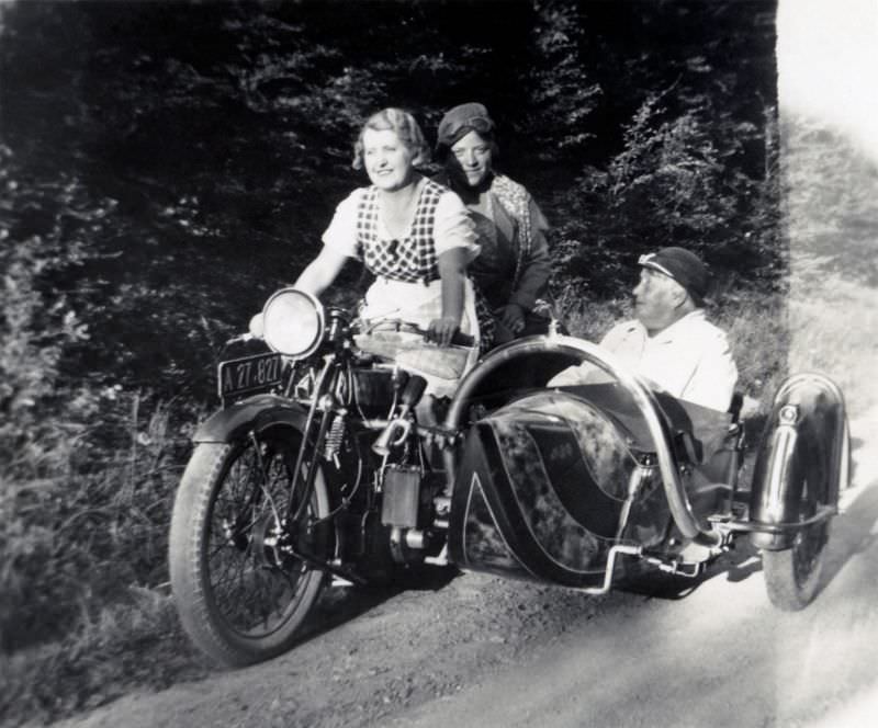 A company of three posing with a ajs sidecar motorcycle on a dirt road in the countryside. The bike is registered in the city of vienna, circa 1935.