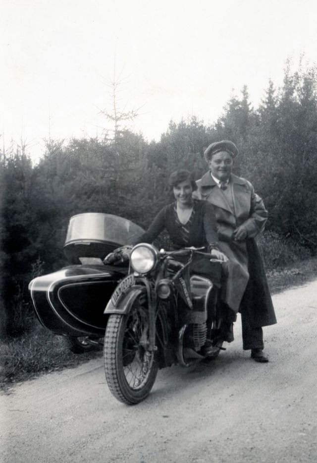 A lady in an elegant dress and a fellow in a leather coat posing with a bmw r 11 combination on a gravel road in the countryside. The vehicle is registered in the city of munich, circa 1935.