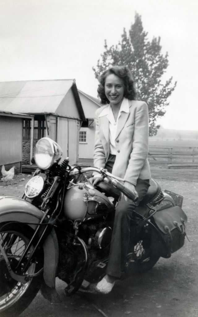 A cheerful young lady in a white sports coat posing in the saddle of a harley-davidson wl 750, circa 1948.
