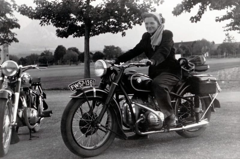 A young lady with a scarf wrapped around her head posing in the saddle of a bmw r 51/3, may 17, 1952.