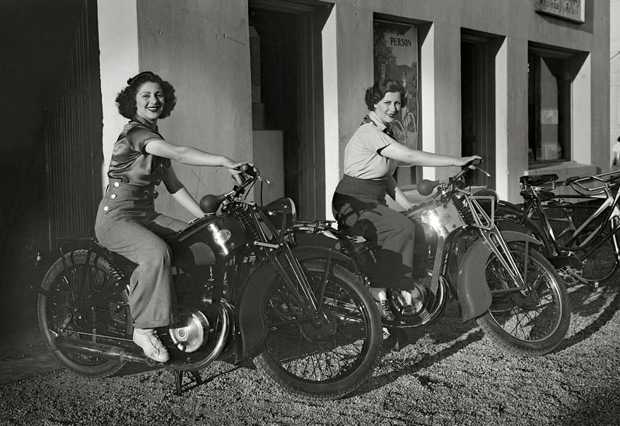 A couple of ladies astride a couple of vintage motorcycles