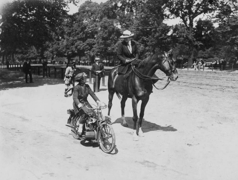 A woman riding a motorcycle alongside a woman on a horse in london, 1921.