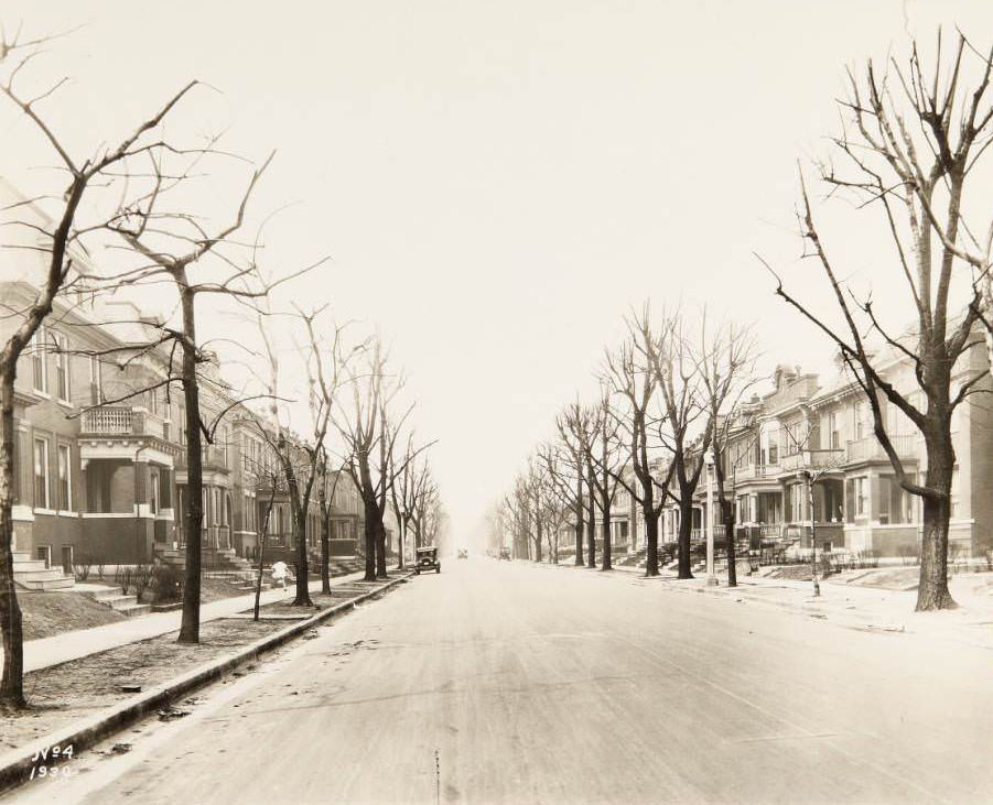 Residential street in St. Louis, with a child in a white outfit running along the sidewalk, 1930