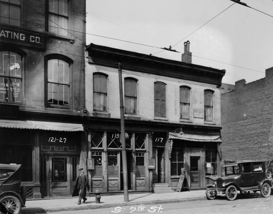 View of several storefronts on the 100 block of South 7th Street between Walnut and Elm. Keystone Lubricating Company, St. Louis Wholesale Drug Company, and James Robinson's restaurant are visible, 1930