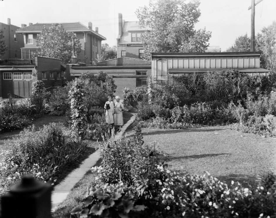 View of backyard garden at 5228 Westminster Place in Central West End, with two women and a small black dog visible, 1931