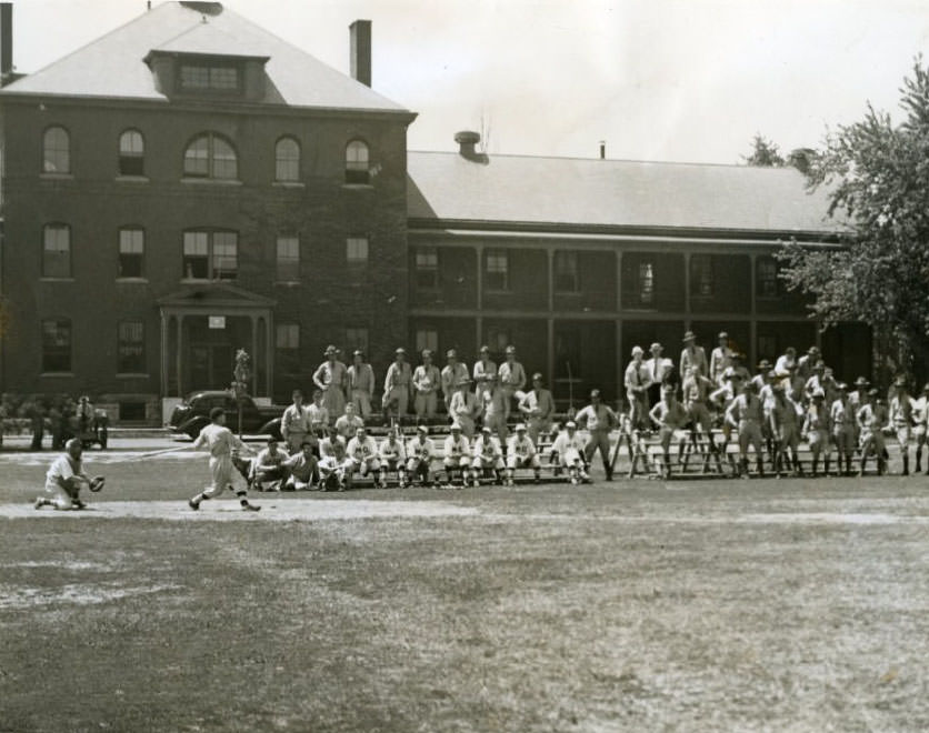 Private dressed in baseball clothes plays a game while fellow soldiers watch in 1937.