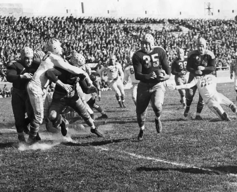 Green Bay Packers' attack blocks Gunners, with Full Back George Balazs clearing a path as Packers Mates Ray Goldenberg and Larry Craig shove Guard Tiger Flowers, 1930