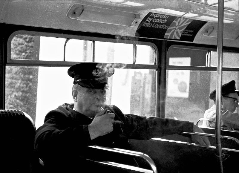 Weary regulator enjoys a well-deserved pipe in a waiting bus, Paignton bus station, 1970