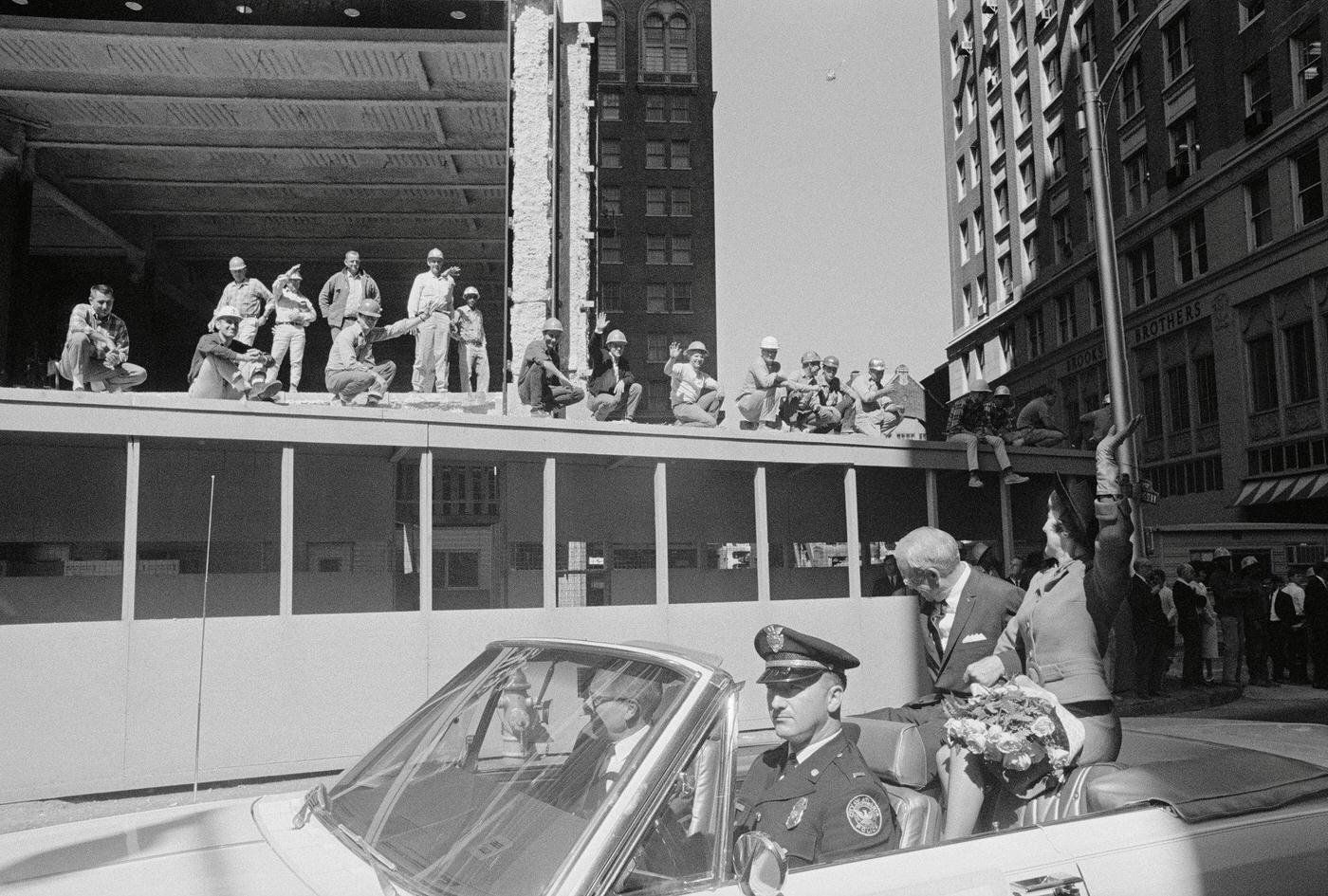 A group of construction workers takes time off to wave to actress Olivia de Havilland (far right) passing in an open car with Atlanta Mayor Ivan Allen, 1960s