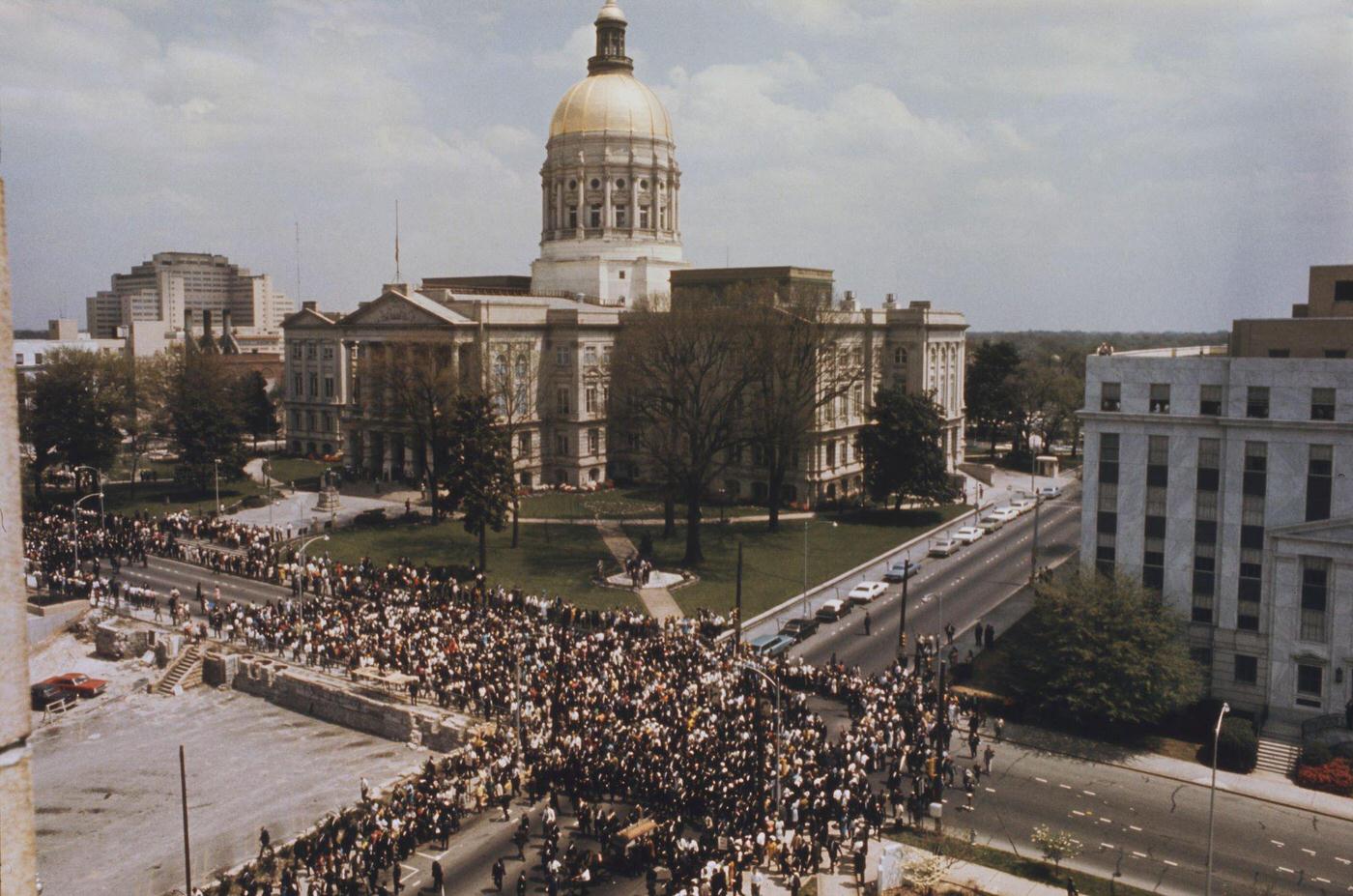 Funeral of assasinated American minister and civil rights leader, Martin Luther King with mourners following the funeral wagon carrying the casket past the state capitol building in Atlanta, Georgia on 9th April 1968.