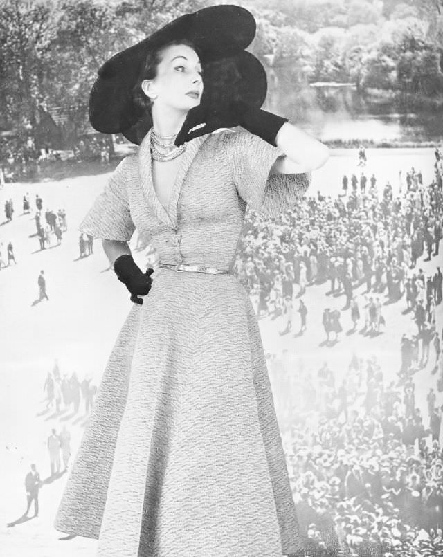 Barbara Goalen in pale silvery faille dress with silver belt and black tulle petalled hat by Molyneux, 1950.