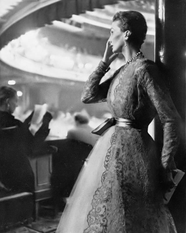 Barbara Goalen in ballerina-length dress in pale caramel tulle, over it a coat of deep coffee lace fastened with a turquoise satin sash by Harald after Dior, 1951.