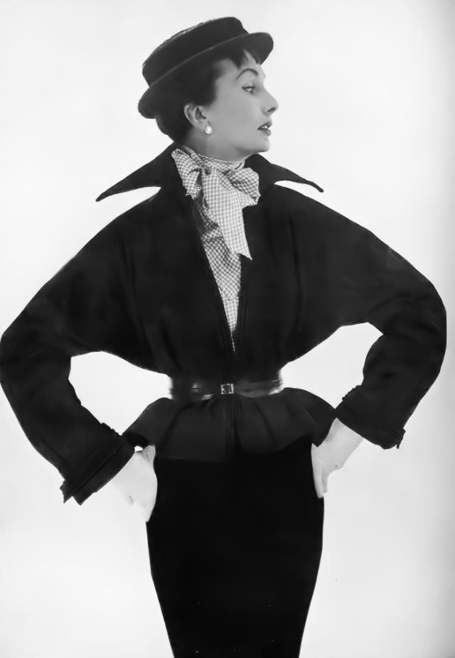 Barbara Goalen in black poult jacket, bloused, belted and high-collared, over mauve-and-white checked shirt and wine-red boater, by Victor Stiebel, 1950.
