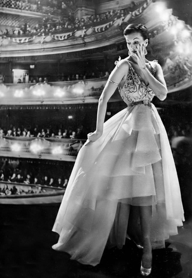 Barbara Goalen in filmy white organdie dress with a low-backed bodice glittering with sequins and a tiered skirt dipping behind by Harald, 1950.