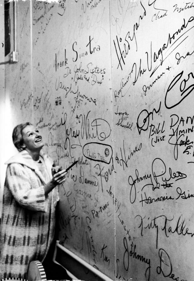 Phyllis Diller read the names of the well-known (including Frank Sinatra, Vic Damone and the Vagabonds) and the not so well-known on a wall after circling her own name (center), 1963.