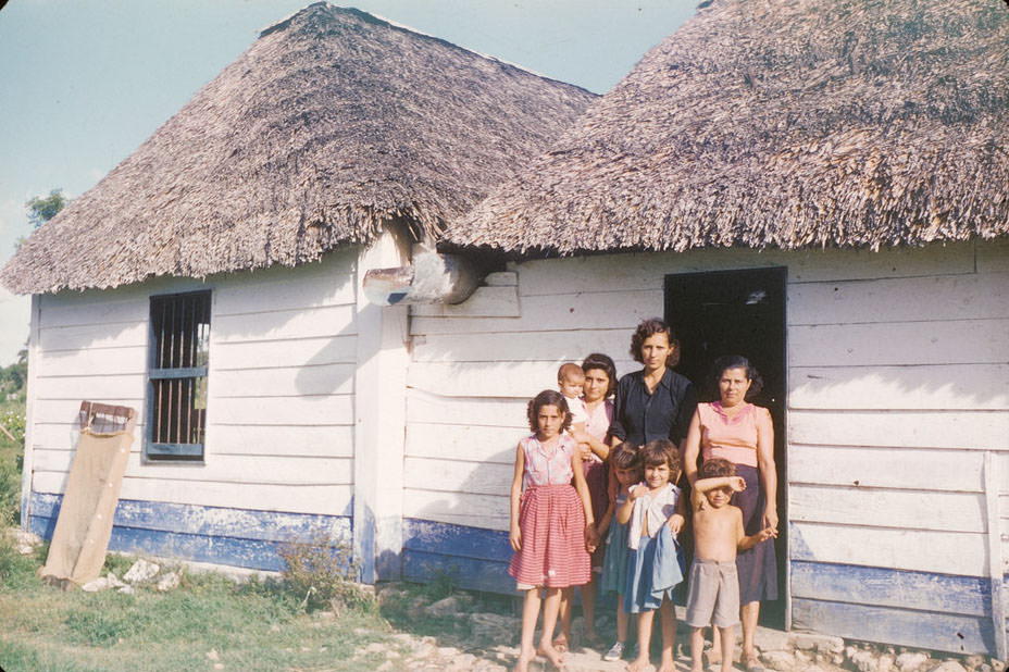 Cuban family in front of blue and white house with thatched roof