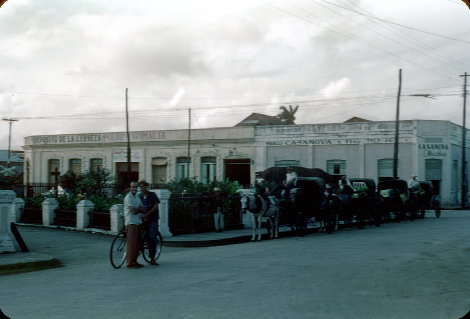Horse drawn taxis parked by plaza, Casanova store, Sagua La Grande
