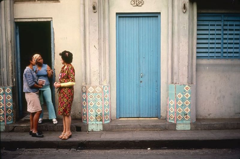 A trio of women stand and talk in a doorway decorated with colorful tiles, Old Havana.