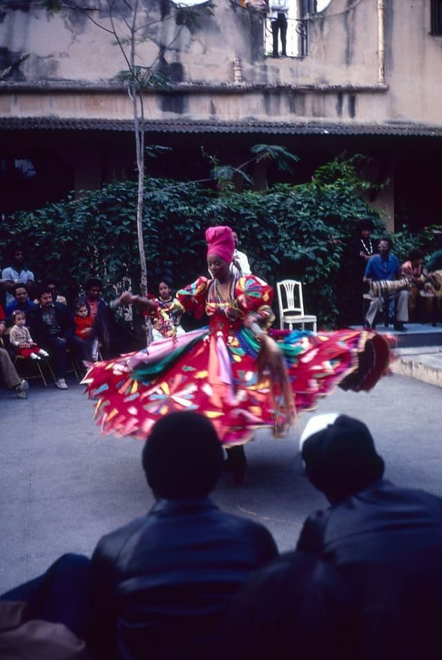 The audience watch a woman in a colorful dress and headdress dances in Plaza Vieja to a live band, Havana, Cuba.