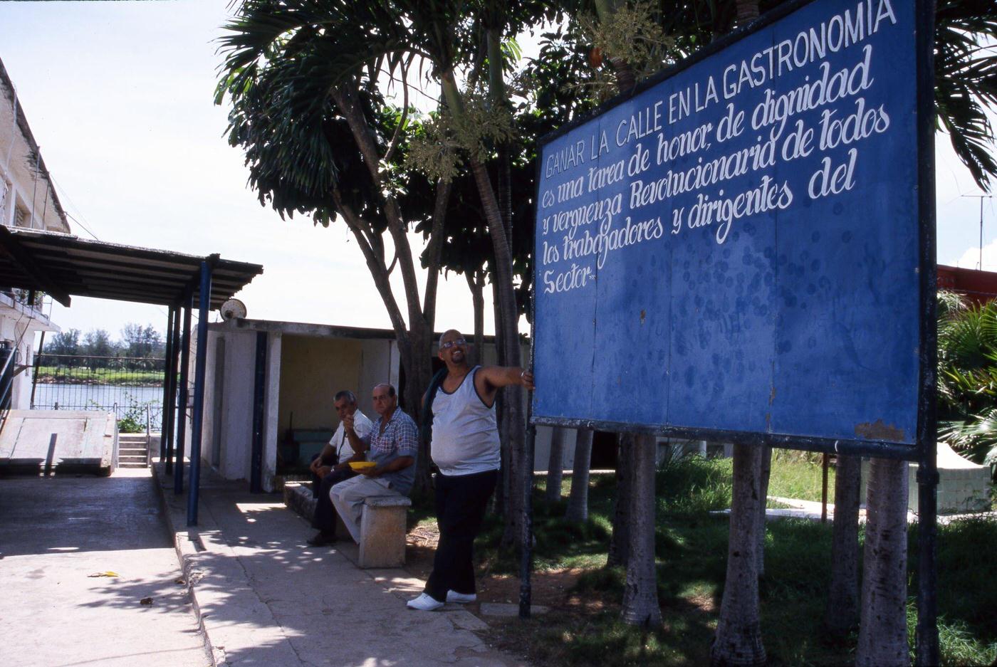 Workers waiting for a bus in front of a poster honoring the value of work in Havana, Cuba, June 1999.